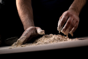 Male hands knead pizza dough on a dark background.