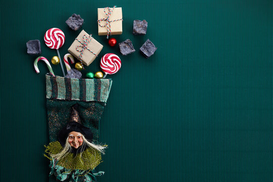 Befana sock with sweet coal and candy on dark greeen background. Italian Epiphany day tradition.