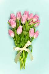 Bouquet of pink tulips with satin ribbon on a blue background. Mother's Day, Easter, Valentine's Day. Spring flowers. Vertical photo