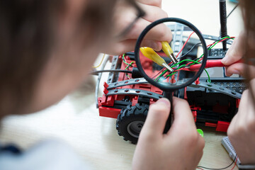 close-up of a magnifying glass in a child's hand. Teenager boy at robotics school makes robot managed from the constructor, child learns robot constructing. © Oksana Klymenko