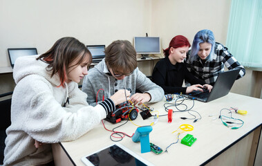 Diverse teen pupils build robot vehicle learning at table at STEM engineering science education class.