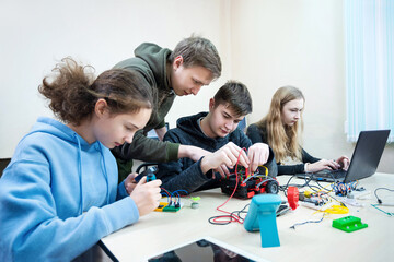 Diverse teenager pupils build robot vehicle learning at table at STEM engineering science education class.