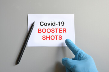 the hand of the doctor with the blue glove writes on white paper the text 'Covid-19 Booster...