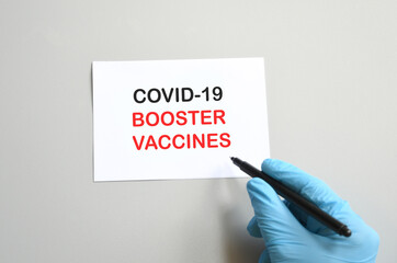 the hand of the doctor with the blue glove writes on white paper the text 'Covid-19 Booster...