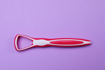 Red tongue cleaner on violet background, top view