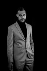 black and white portrait of a young businessman in a gray suit and black turtleneck, looking serious with an hand in his pockets