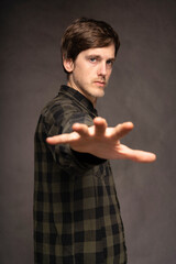 Young handsome tall slim white man with brown hair reaching out with his hand with flannel shirt on grey background