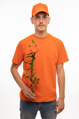 Young handsome tall slim white man with brown hair holding orange flower with orange shirt and orange cap isolated on white background