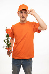 Young handsome tall slim white man with brown hair fixing his cap holding orange flower with orange shirt isolated on white background