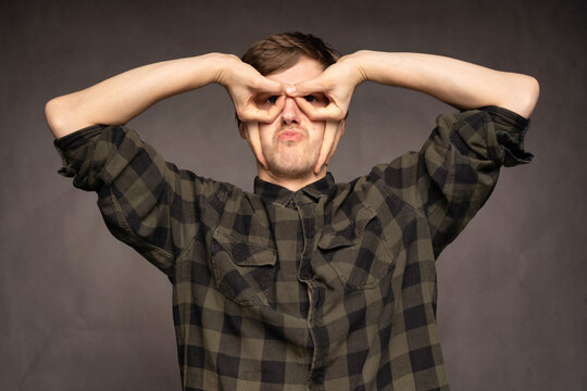 Young Handsome Tall Slim White Man With Brown Hair Making Glasses Out Of His Hands With Flannel Shirt On Grey Background