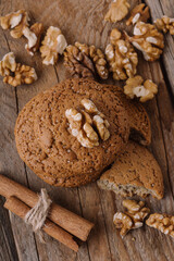 Fototapeta na wymiar Stack of oatmeal cookies with walnuts on wooden background. Healthy homemade sweets. Broken cookie. Cookie recipe with nuts and cinnamon. Vertical