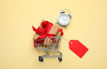 Shopping cart with tag, gift box and alarm clock on beige background, flat lay © New Africa
