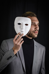 portrait of a serious young man holding a white mask in his hand, concept for being authentic and...