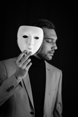 portrait of a serious young man holding a white mask in his hand, concept for being authentic and not showing a face of circumstance, but being truly himself