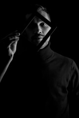 black and white portrait of a young man holding a frame in front of his face, concept for the uniqueness of individuals