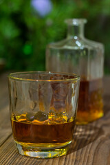 Vertical photo of a glass of whiskey on an old textured wooden table, against the background of a Christmas tree and bottle with alcohol in defocus