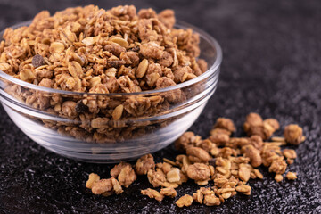 Healthy homemade muesli in a glass bowl on a black background.
Close-up.