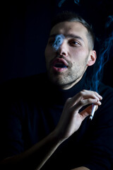 portrait of a concentrated young man making smoke rings with cigarette on a black background