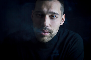 portrait of a young man who is exhaling the smoke of a cigarette from his mouth