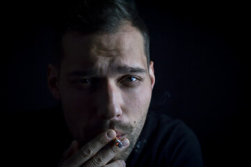 close up portrait of a young man who is smoking holding the last few hits of the cigarette in his hand