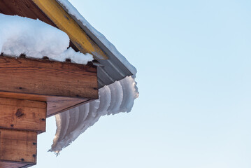 Snow and icicles with ice are sliding from the roof of the house.