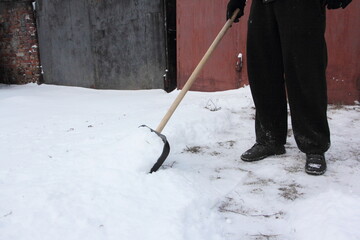 A man cleans snow with a shovel in front of the garage gate in winter