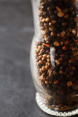 A mixture of seasonings, spices and herbs in a glass mill on a black background.