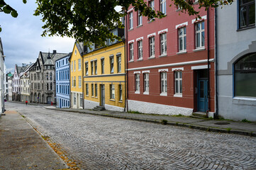 Naklejka premium Empty street with colorful houses in the city of Alesund, Norway. Leaves of a tree are framing the picture. No people are on the road due to the Corona pandemic. 
