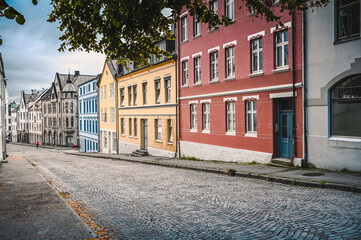 Fototapeta na wymiar Empty street with colorful houses in the city of Alesund, Norway. Leaves of a tree are framing the picture. No people are on the road due to the Corona pandemic. 