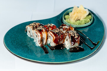 sushi roll with eel philadelphia cheese sprinkled with sesame seeds on a blue plate with ginger and wasabi sauce on a white plate
