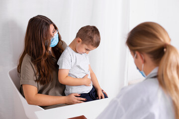 Young brunette woman with little boy having consultation at pediatrician office. Child has...