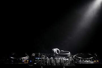 Modern DJ controller and headphones under beam of light on black background