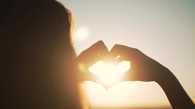 Girl folded her hand heart at sunset.Silhouette of girl in nature.Fingers in shape of heart in rays of sun.Girl stretched out her hand to sky at sunset.Silhouette of man in nature.Love nature concept