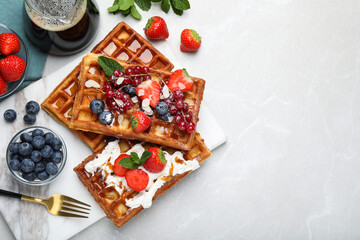 Board with delicious Belgian waffles, berries and whipped cream on light marble table, flat lay....