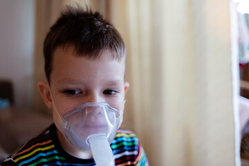 Child holds a mask vapor inhaler. Sick Caucasian boy using inhaler containing medicine to stop...