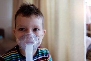 Child holds a mask vapor inhaler. Sick Caucasian boy using inhaler containing medicine to stop...