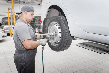 Mechanician changing car wheel in auto repair shop.