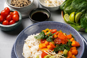 A blue bowl with red thai vegetable curry and basmati rice, fresh lime, cilantro, spinach, chilli peppers and cherry tomatoes