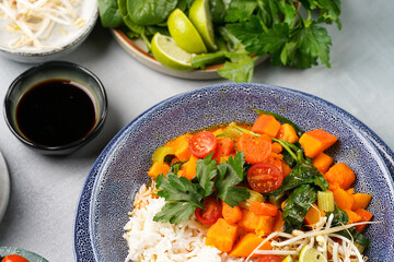 A blue bowl with red thai vegetable curry and basmati rice, fresh lime, cilantro, spinach, chilli peppers and cherry tomatoes
