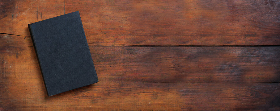 Closed old black book on a table. Blank cover notebook on wooden background, top view. Copy space