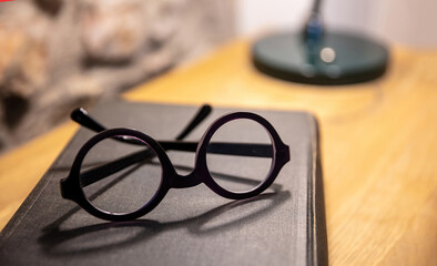 Eyeglasses and an old black book on a wooden table. Teacher doctor office desk. Study room, library