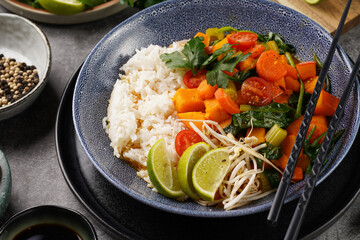 A blue bowl with red thai vegetable curry and basmati rice, fresh lime, cilantro, spinach, chilli peppers and cherry tomatoes