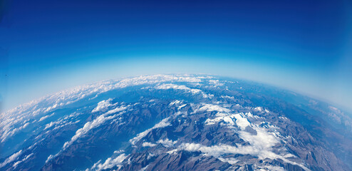 Curvature of planet earth. Aerial view. Blue sky over snowed mountain peaks. Space, science concept
