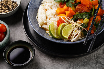 A blue bowl with red thai vegetable curry and basmati rice, fresh lime, cilantro, spinach, chilli peppers and cherry tomatoes