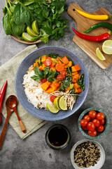 A blue bowl with red thai vegetable curry and basmati rice, fresh lime, cilantro, spinach, chilli peppers and cherry tomatoes, top view