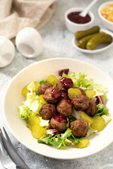 Swedish meatballs with salad, pickled cucumber and lingonberry jam in a bowl. Traditional Scandinavian dish in a ceramic plate on a light gray culinary background closeup	
