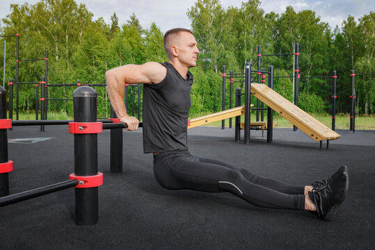 Young fit man doing triceps dips exercises during outdoor cross training workout.