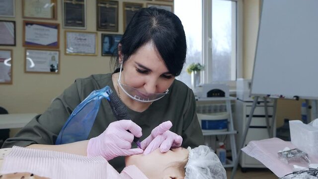 Beautician at work. Beautician wearing a protective mask applies a permanent pigment tattoo to women's lips with a tattoo needle in a salon