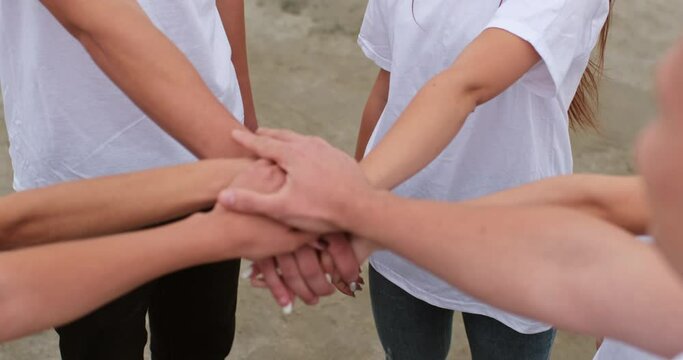 People in white T-shirts put their hands together in the center of the circle, unite their team, support each other.