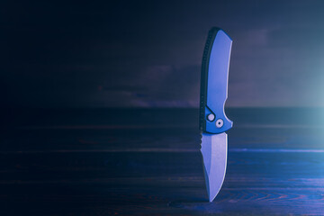 Pocket knife for EDC or Everyday Carry on wooden background with copy space. Automatic folding knife photo in dark low key.